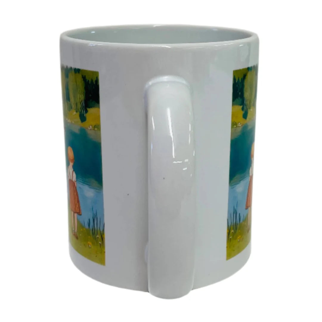 The “Children by the Lake in Summer Coffee Mug” is a white ceramic mug featuring Carl Larsson’s illustration of a girl in a red dress by a lake, with part of the scene hidden behind the handle.