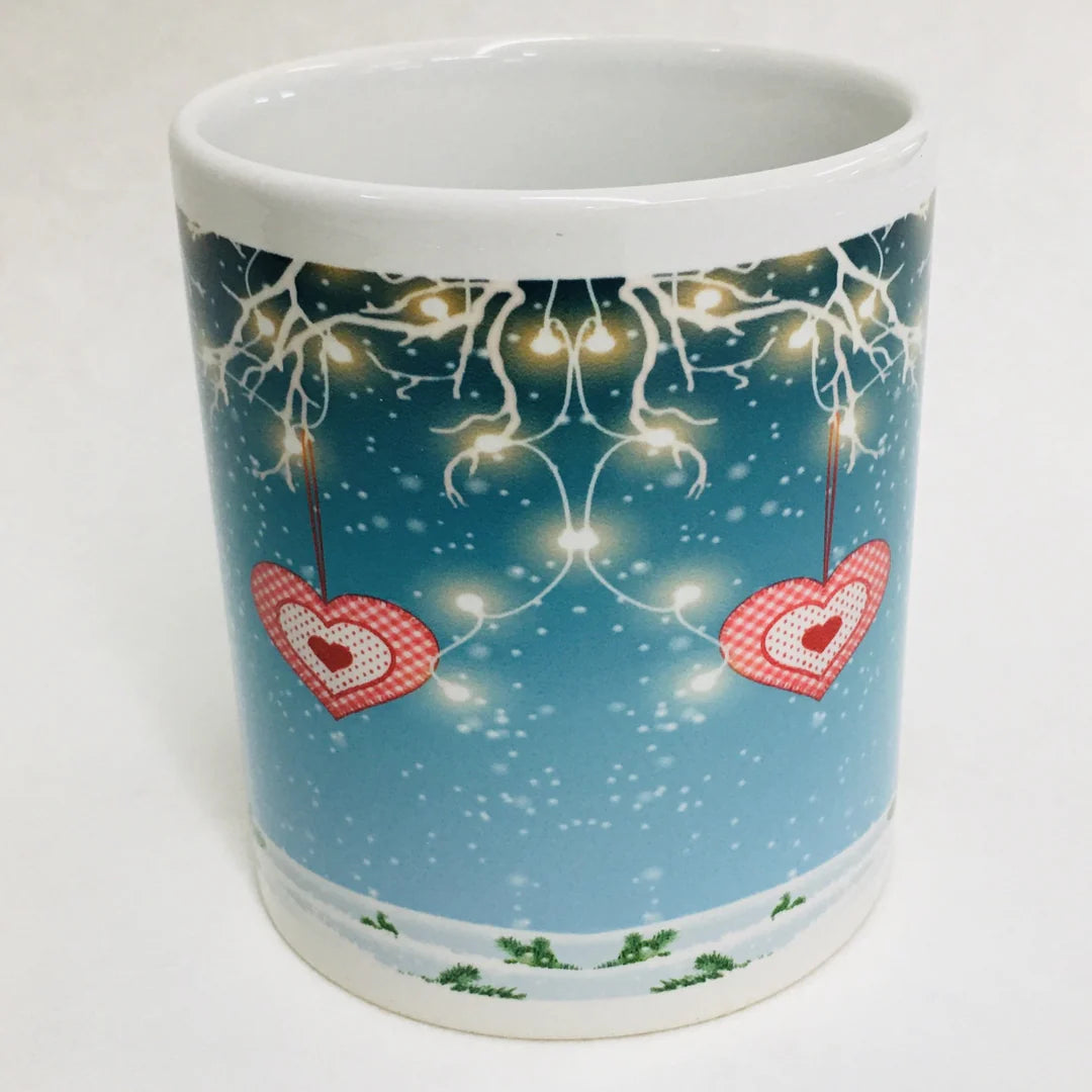 Enjoy cozy moments with this 11 oz white ceramic coffee mug featuring a gnome holding string lights, festive tree branches, and two red heart ornaments on a snowy blue background—a charming winter-themed mug.