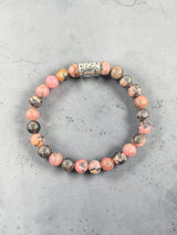 Bracelet featuring an Algiz rune charm, pink and brown marbled stones, and one ornate silver bead, shown on a gray stone background.