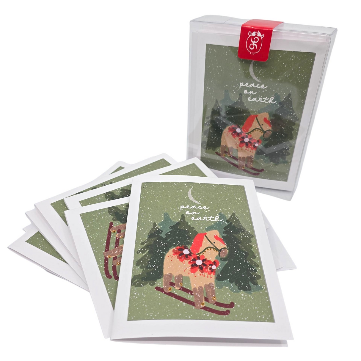 A set of 8 blank cards and envelopes, "Card Pack: Dala Horse on Skiis ‘Peace on Earth’" by Lisa Rydin Erickson, features a Scandinavian design with a Dala horse on skiis and pine trees. Cards are partially stacked beside a clear box.
