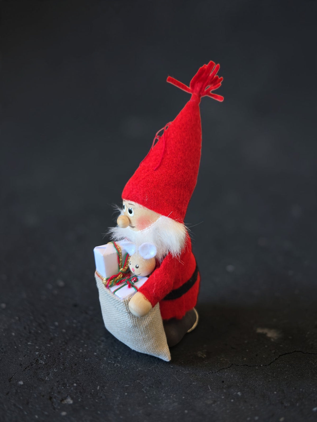 A Scandinavian Santa Tomte figurine wearing a red felt hat and suit, holding a gift sack containing a small mouse toy.
