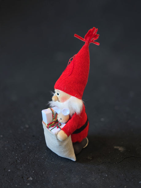 A Scandinavian Santa Tomte figurine wearing a red felt hat and suit, holding a gift sack containing a small mouse toy.