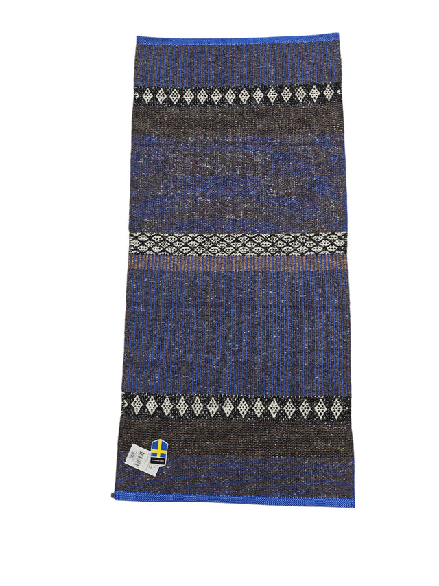 The Cotton/Vinyl Rug: Horredsmattan - Mixed Forest - Cobalt features blue, black, and white stripes with diamond patterns, shown flat with a Swedish flag label in the bottom left corner.