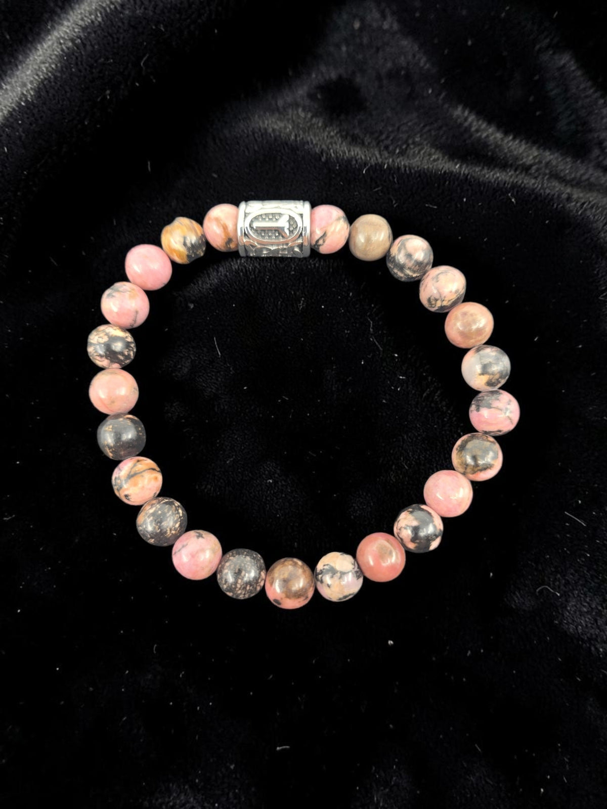 Bracelet with pink and gray marbled stones and a silver clasp, shown on a black velvet background.