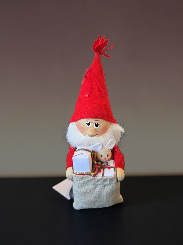 Nordic gnome figurine wearing a red pointed hat and holding a fabric sack filled with small gifts and a miniature toy rabbit.