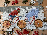 Completed puzzle with Paul Bunyan and his blue ox riding a tandem bicycle with saw blade wheels; several edge pieces are missing.
