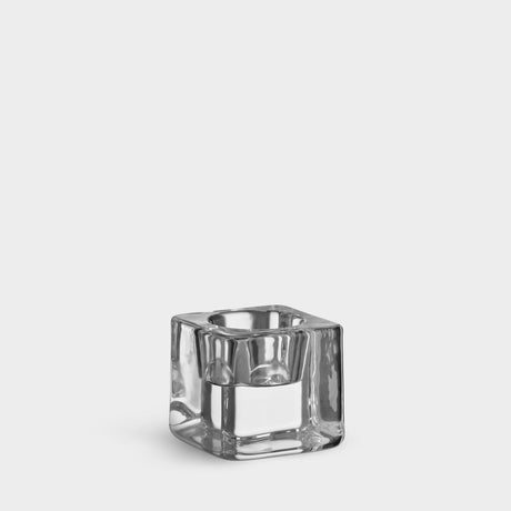 The Orrefors Ice Cube Votive Candle Holder by Goran Warff, crafted from clear crystal and shaped for tealight candles, sits elegantly on a plain white background.