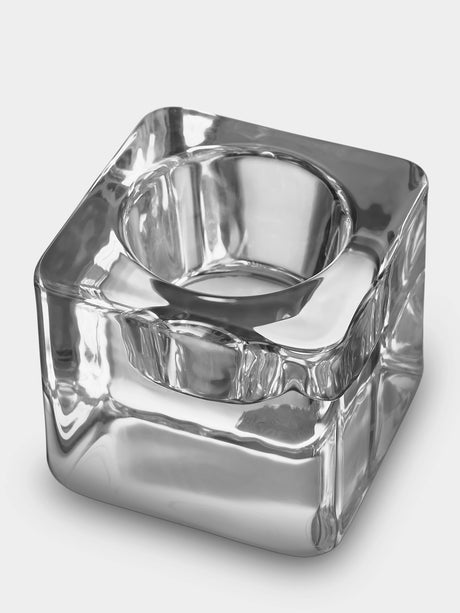 The Orrefors Ice Cube Votive Candle Holder by Goran Warff features a clear crystal square base with a circular center, designed to elegantly hold tealight candles or serve as a stylish ashtray with grooves for resting cigarettes.