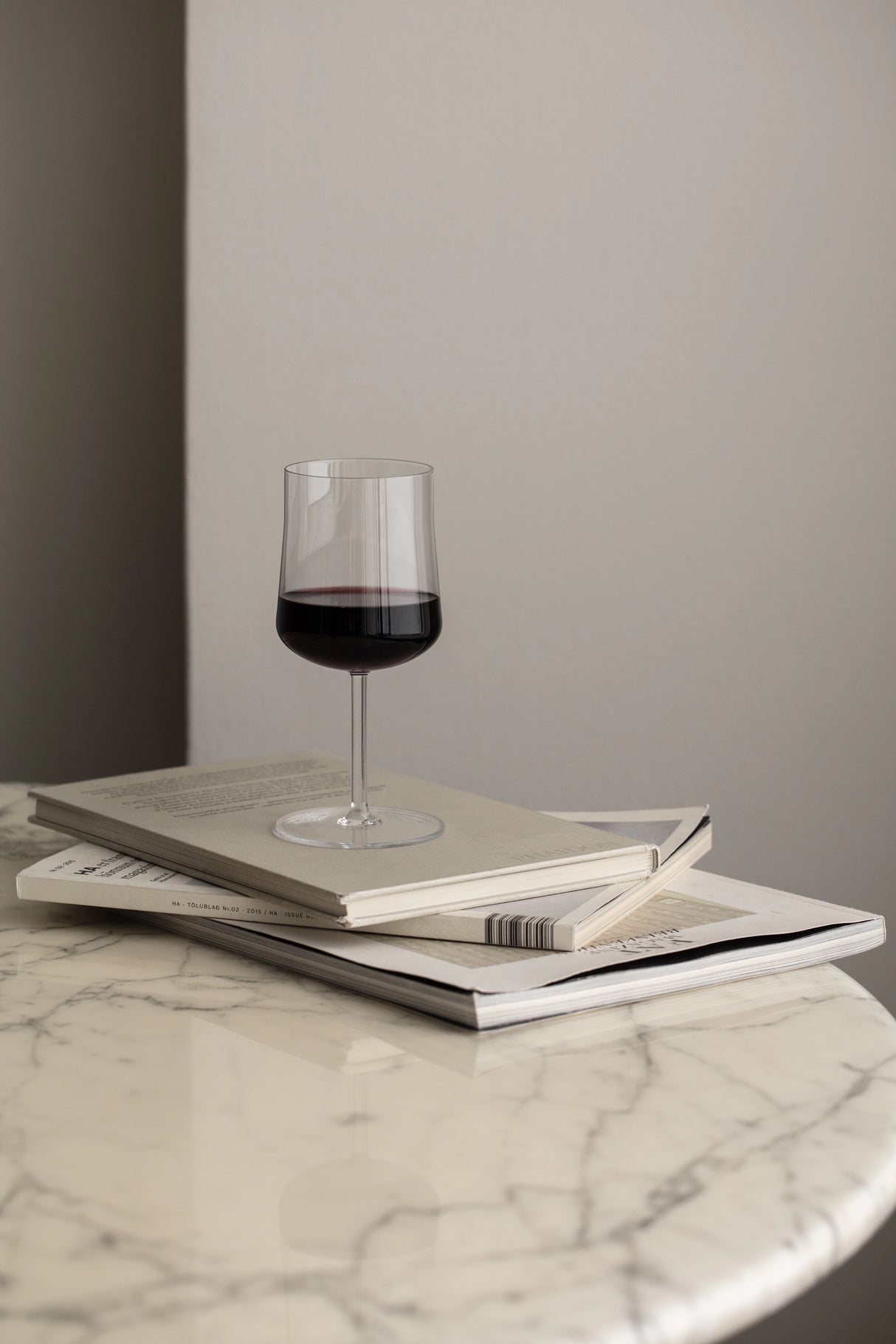 An Orrefors: Informal Medium Glass 12oz from a 2-Pack elegantly sits on three stacked books on a round marble table, highlighting exquisite Scandinavian design.