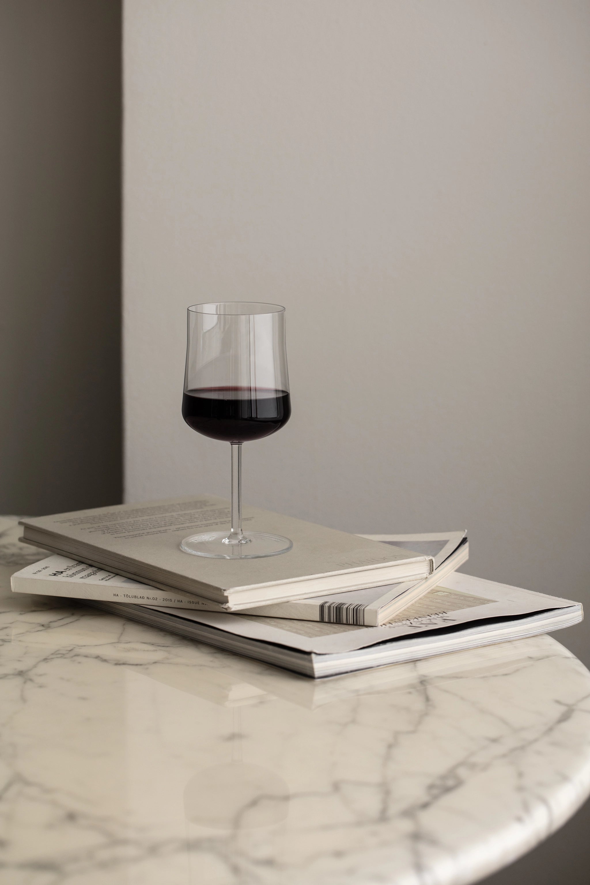 An Orrefors: Informal Medium Glass 12oz from a 2-Pack elegantly sits on three stacked books on a round marble table, highlighting exquisite Scandinavian design.