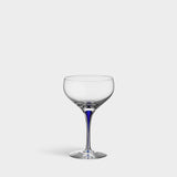 An Orrefors: Intermezzo Blue Coupe Glass 10oz with a dark blue stem elegantly stands against a plain white background.