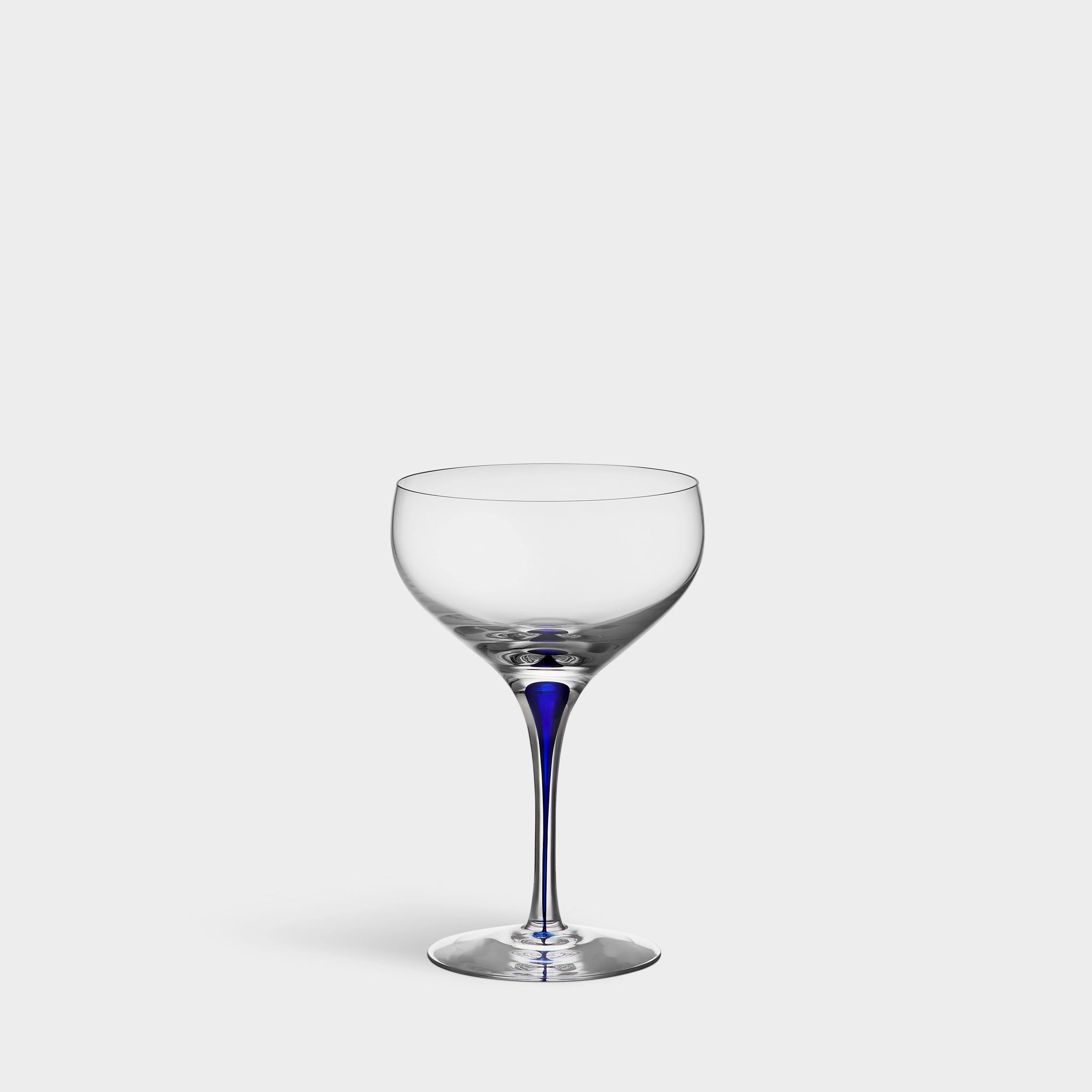 An Orrefors: Intermezzo Blue Coupe Glass 10oz with a dark blue stem elegantly stands against a plain white background.