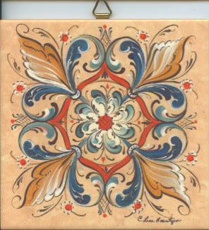 The 6" Ceramic Tile, Lise Lorentzen Rosemaling features a square ceramic design with symmetrical floral and leaf patterns in blue, brown, red, and beige, inspired by classic Norwegian folk art and rosemaling traditions.