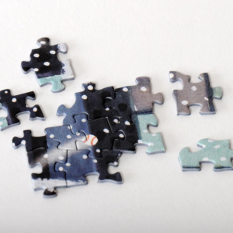 Blue, black, and white jigsaw puzzle pieces on a white surface, some connected and others loose. PuzzleTwist logo visible on a few pieces.