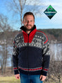 A man stands outdoors in the Nordlys - Classic Norwegian Star Windbreaker sweater (Navy/Red), with trees and water in the background. The Windbreaker label is in the top right corner.