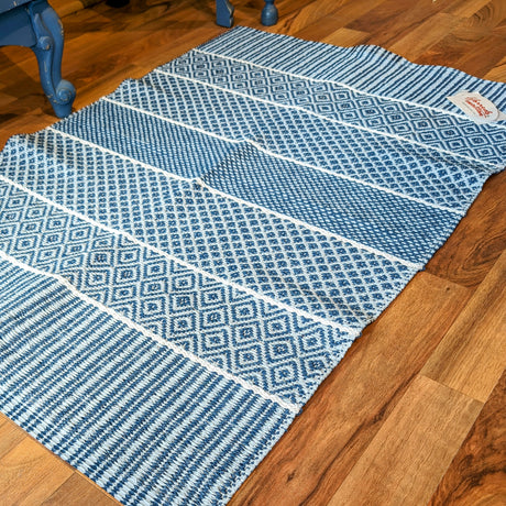 The Vinyl Rug: Horredsmattan - Alfie - Blue, featuring geometric patterns, is elegantly placed on a wooden floor beside a blue chair.