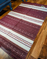 The Vinyl Rug: Horredsmattan - Astor - Red, featuring decorative maroon and white stripes, is laid out on a wooden floor.