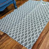Eye Grey rug (70x100cm) with a reversible non-skid design, showcasing a white and gray diamond pattern on a wooden floor.