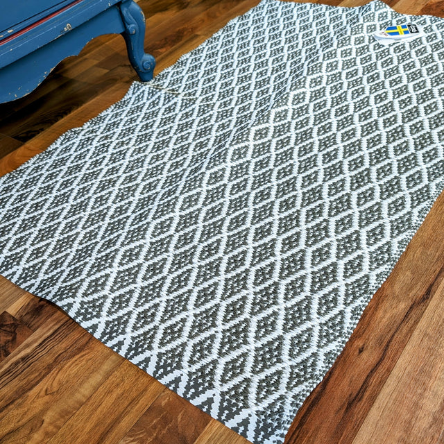 Eye Grey rug (70x100cm) with a reversible non-skid design, showcasing a white and gray diamond pattern on a wooden floor.