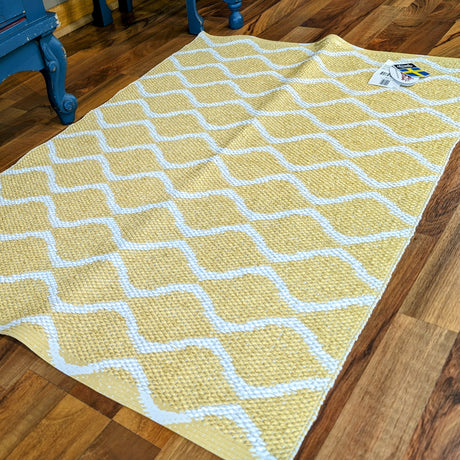 A Horredsmattan vinyl rug with a yellow wavy grid pattern lies on a wooden floor beside blue furniture, highlighting exquisite craftsmanship.