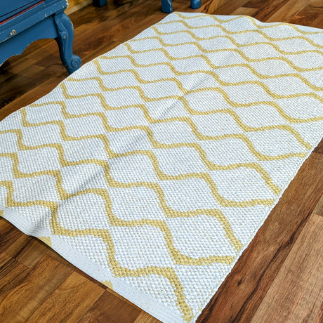 A Horredsmattan Vinyl Rug in yellow with a geometric diamond pattern is placed on a wooden floor next to blue furniture.