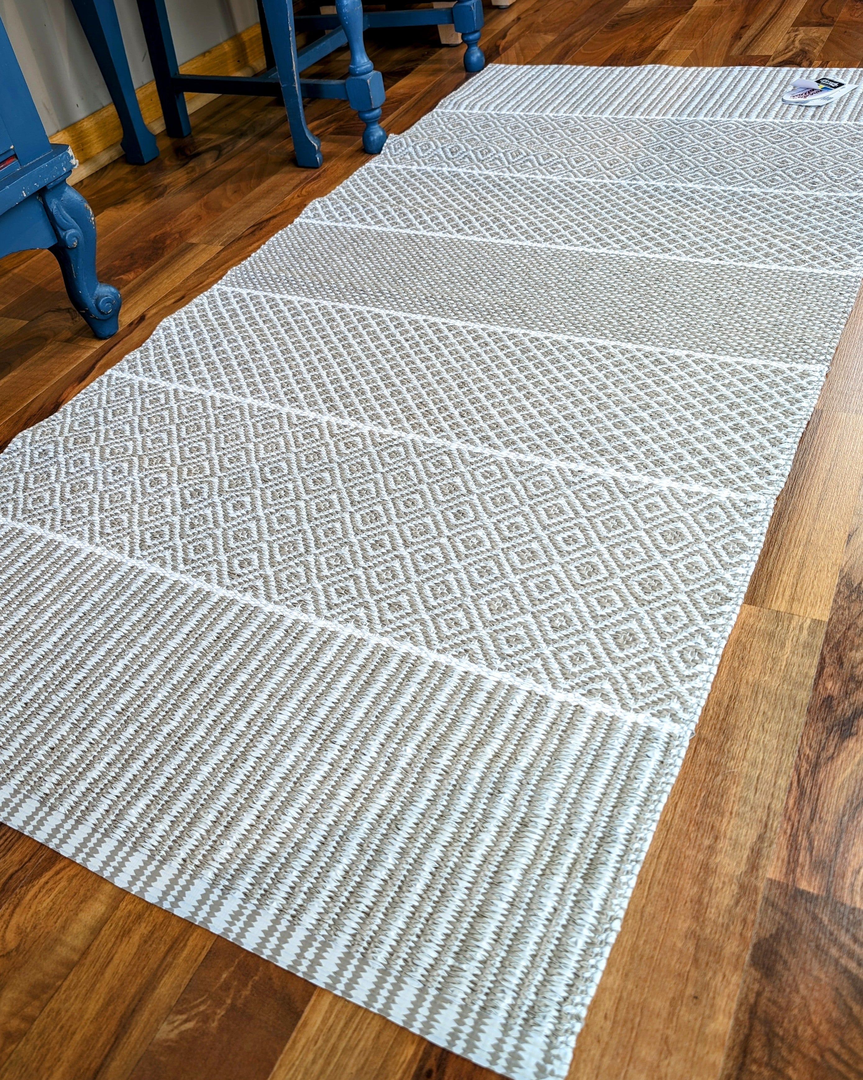 A grey and white patterned Rug: Alfie Sand graces the wooden floor, with a blue table partially visible in the background, capturing a touch of Swedish tradition.