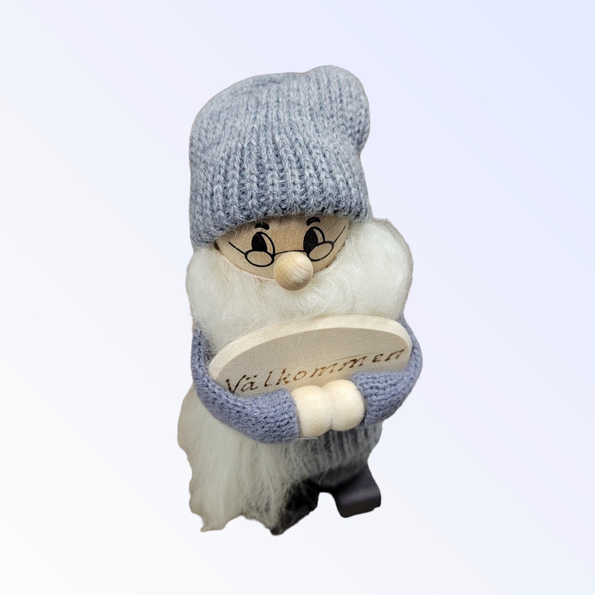The Handcrafted Swedish Santa Figurine wears a gray hat and sweater while holding a wooden Välkommen sign, adding whimsy and warmth to any home.