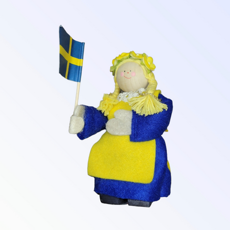 The Figurine: Swedish Girl with Flag artistically captures a girl dressed in traditional Swedish colors as she delicately holds a small Swedish flag.