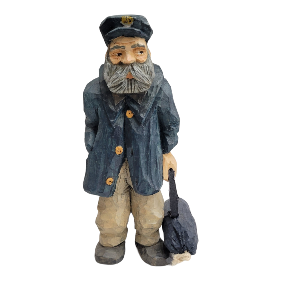 The "Home Port" figurine by Bill Erickson is a hand-carved wooden representation of an old sailor with a gray beard, wearing a navy coat and cap, and holding a bag. This piece beautifully reflects the weathered charm of maritime tales through its artisanal craftsmanship.