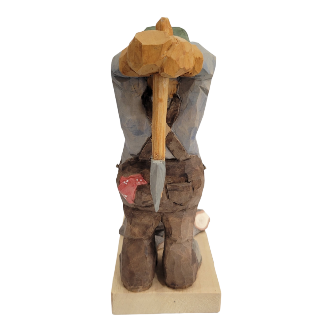 The hand-carved Woodchopper figurine by Bill Erickson portrays a figure facing away, holding an axe, with a small mushroom at their feet on a rectangular base, showcasing craftsmanship akin to Ericksons renowned works.