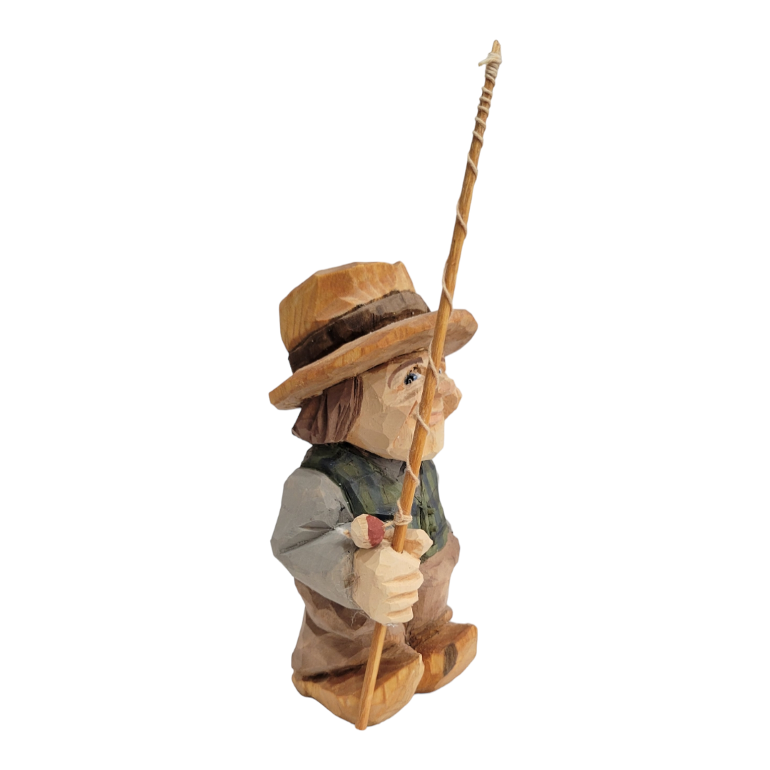 This "Fisherman" figurine by Bill Erickson, hand-painted and wood-carved, features a person in a hat holding a fishing pole, dressed in a vest and boots, set against a white background.