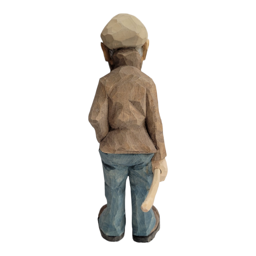 The "Johannes" figurine by Bill Erickson, crafted from wood, depicts a person with their back turned, wearing a hat, brown jacket, and blue pants while holding a tool or stick. This piece beautifully embodies the artisanal craftsmanship for which Bill Erickson is renowned.