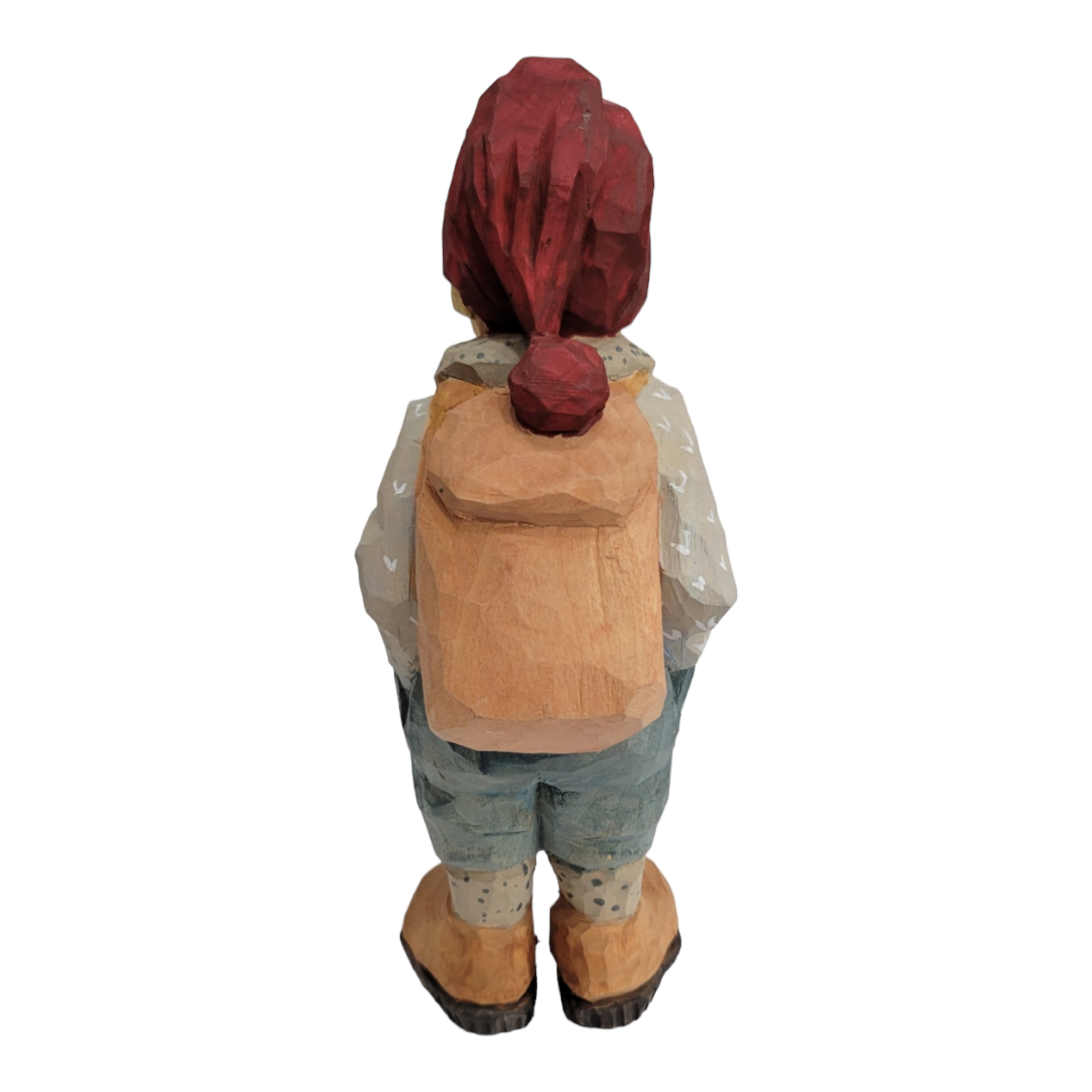 A beautifully hand-carved wooden "Hiker" figurine by Bill Erickson, depicting a person with a red hat, wearing a backpack and casual clothing, facing away.