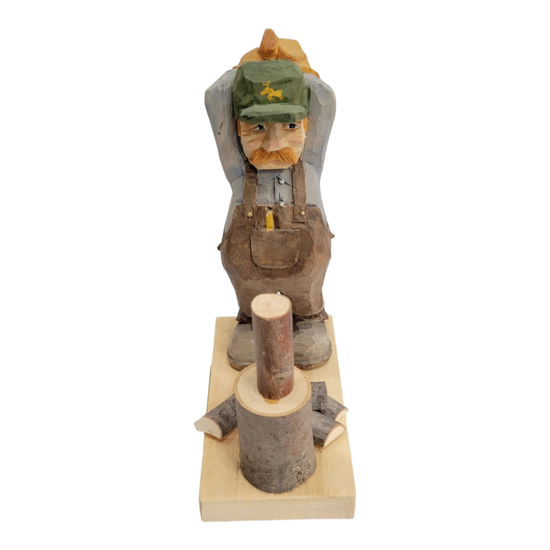 The Woodchopper by Bill Erickson is a hand-carved wooden figurine depicting a man in a green hat and overalls, leaning on an axe beside a log, elegantly poised on a wooden base.