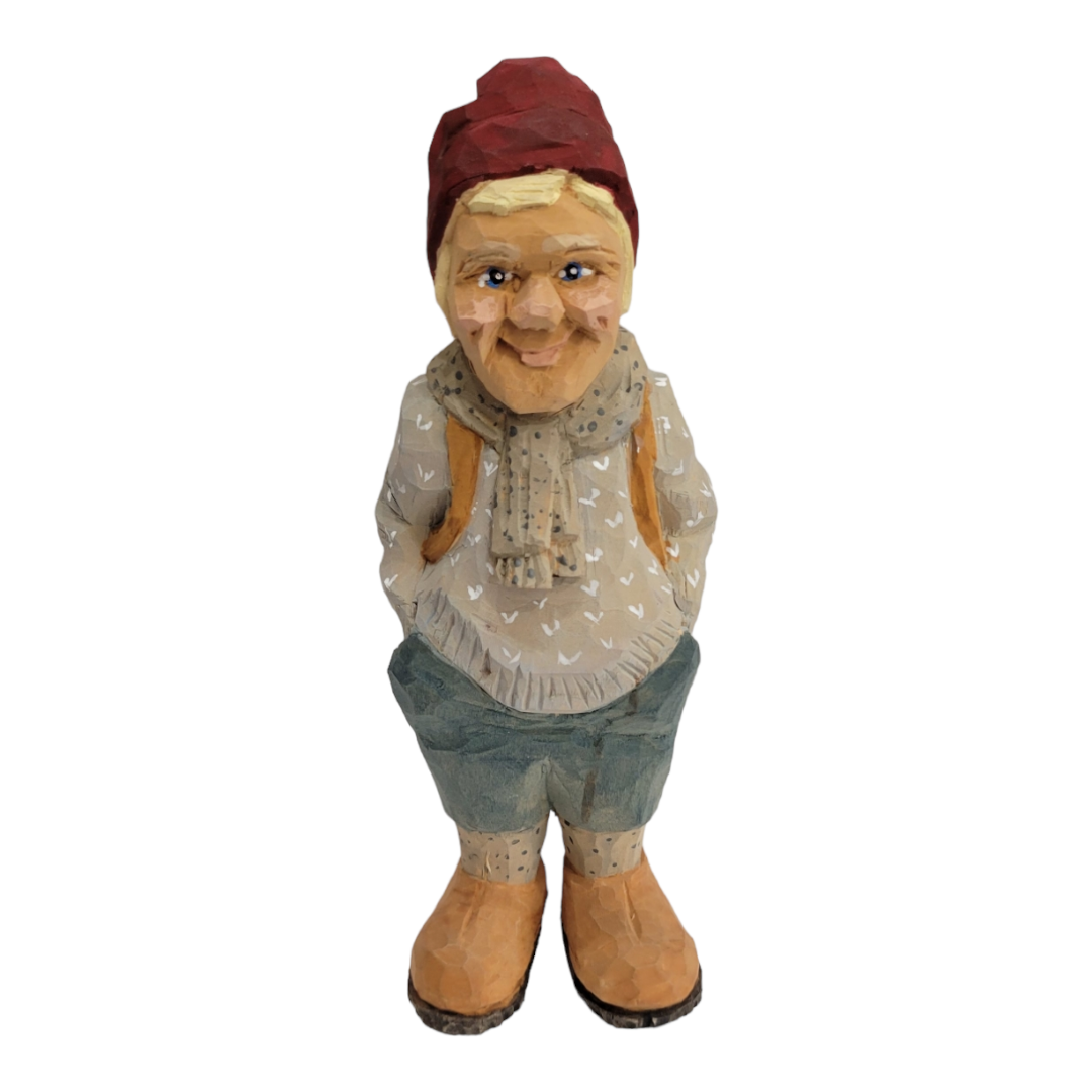 The "Hiker" figurine by Bill Erickson features a hand-carved wood person dressed in a red hat, beige sweater, blue pants, and brown shoes, standing with hands behind their back.