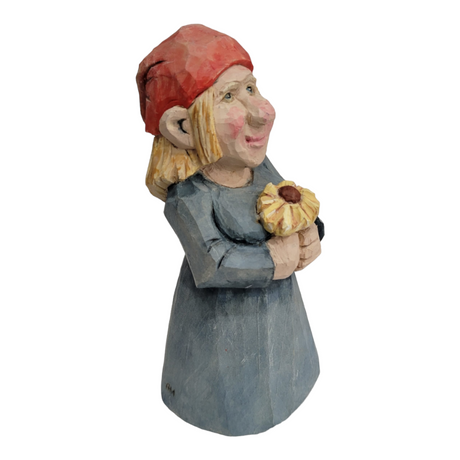 This hand-carved wood figurine, named "Figurine: Woman with Flower," depicts a woman adorned in a red headscarf and blue dress, eloquently holding a small yellow flower.