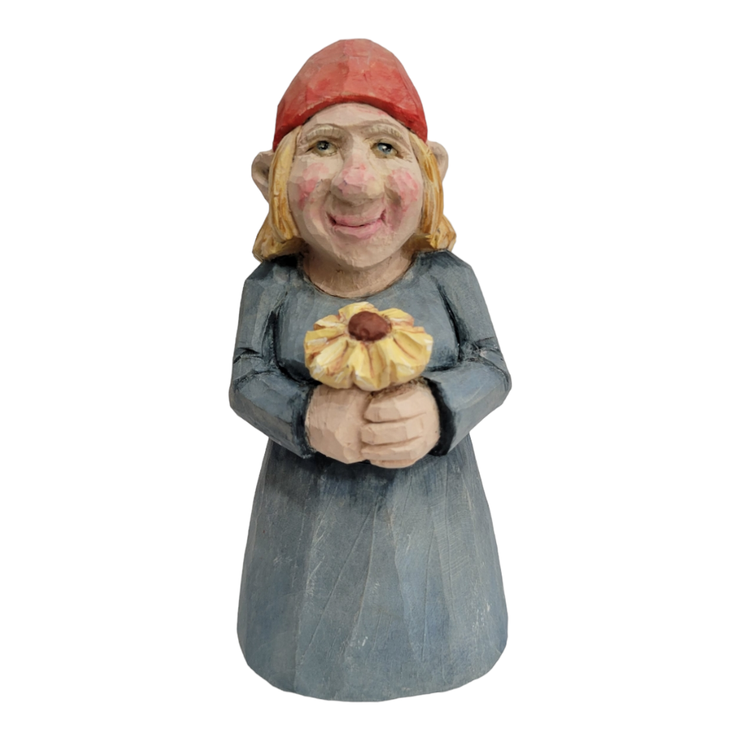 The "Figurine: Woman with Flower" features a hand-carved wood character wearing a red hat and a blue dress, joyfully smiling while holding a yellow flower.