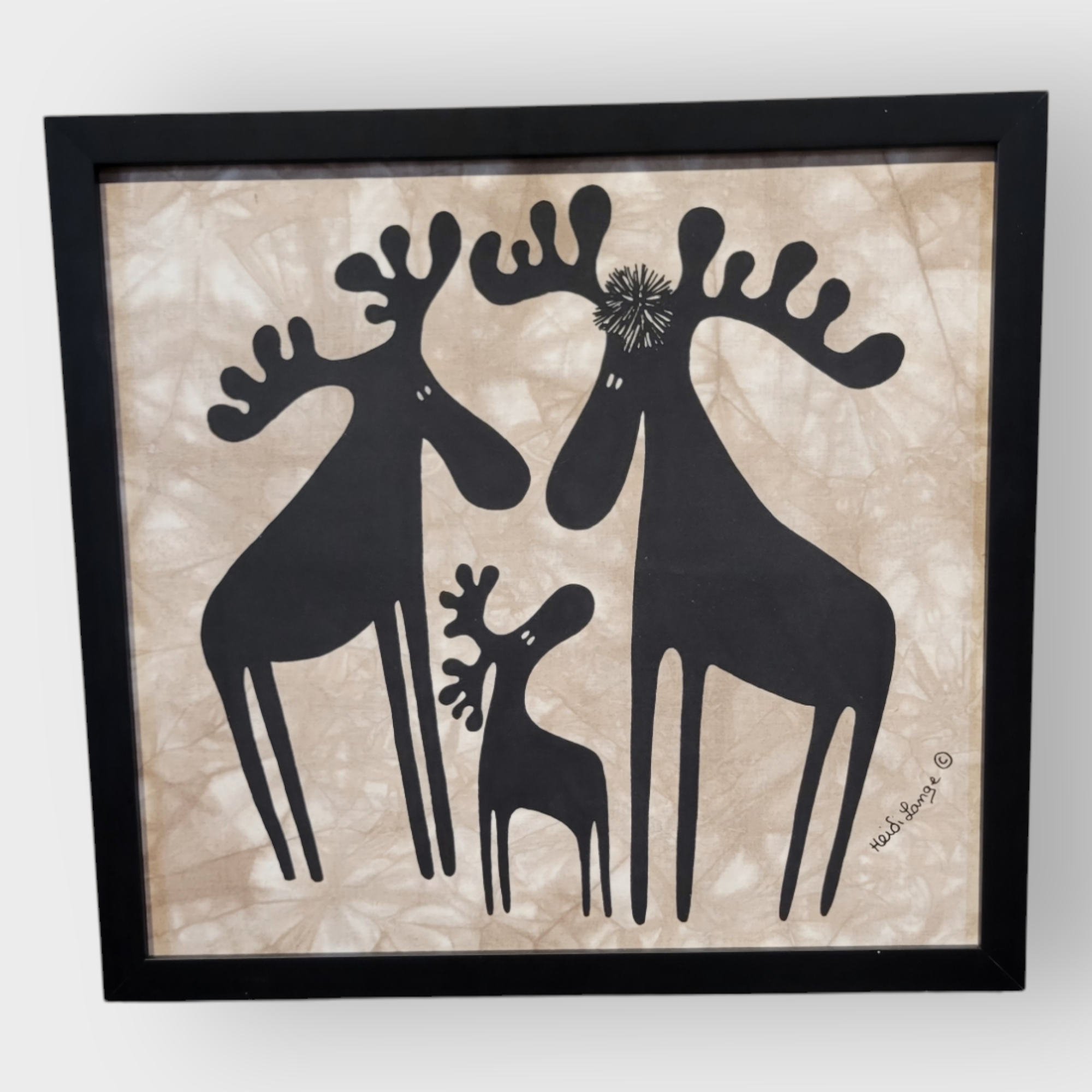 The "Moose Family" artwork by Heidi Lange includes a framed illustration of three stylized, black moose figures against a beige background, measuring 16.5 inches by 15.5 inches, with one smaller moose nestled between two larger ones.