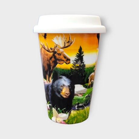 The "Minnesota" Travel Mug (13oz) with lid is a reusable white coffee mug featuring black bear, moose, deer, trees, and flowers against a sunset design.