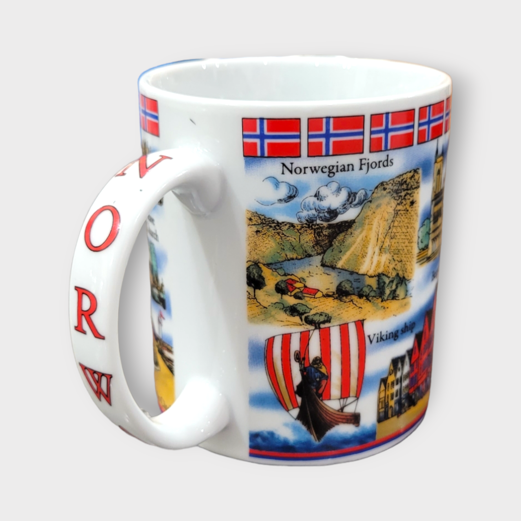 This "Norway" Scenery & Symbols 11oz ceramic mug showcases iconic Norwegian images such as breathtaking fjords, a traditional Viking ship, and the vibrant Norwegian flag, with the handle bearing the word "NORWAY" in striking red letters.