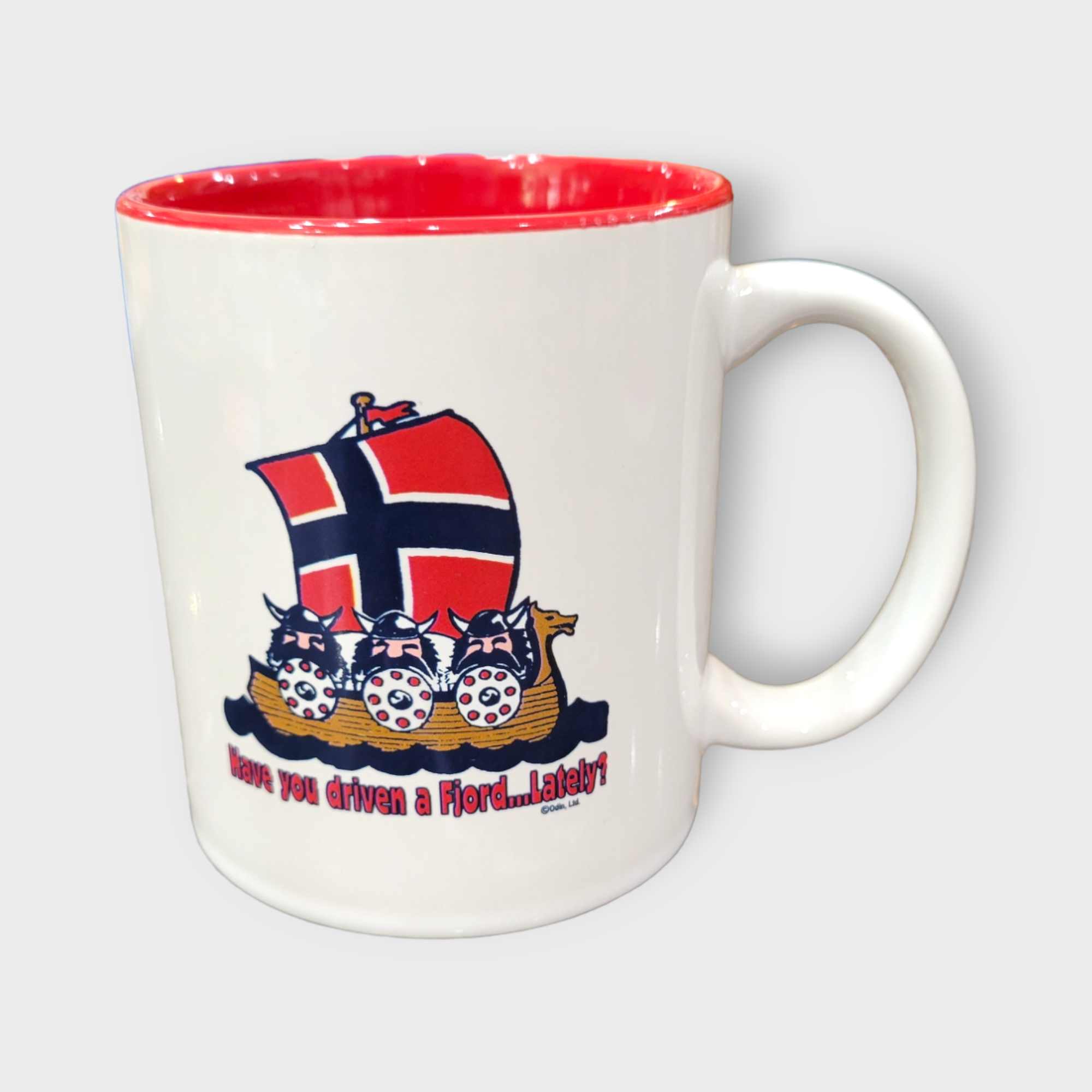 The "Have You Driven A Fjord Lately" mug, with an 11oz capacity, features a red interior and showcases a Viking ship next to the Norwegian flag, along with playful text that adds a whimsical touch.