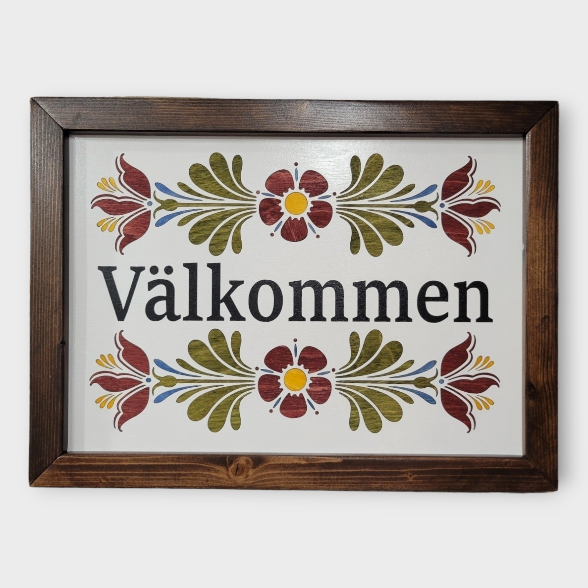 The Valkommen Wall Decor is a laser-etched, framed wood sign that celebrates Swedish heritage with black text and vivid red, green, and yellow kurbits floral designs on a white background.
