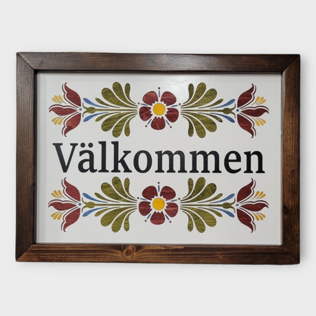 The Valkommen Wall Decor is a laser-etched, framed wood sign that celebrates Swedish heritage with black text and vivid red, green, and yellow kurbits floral designs on a white background.
