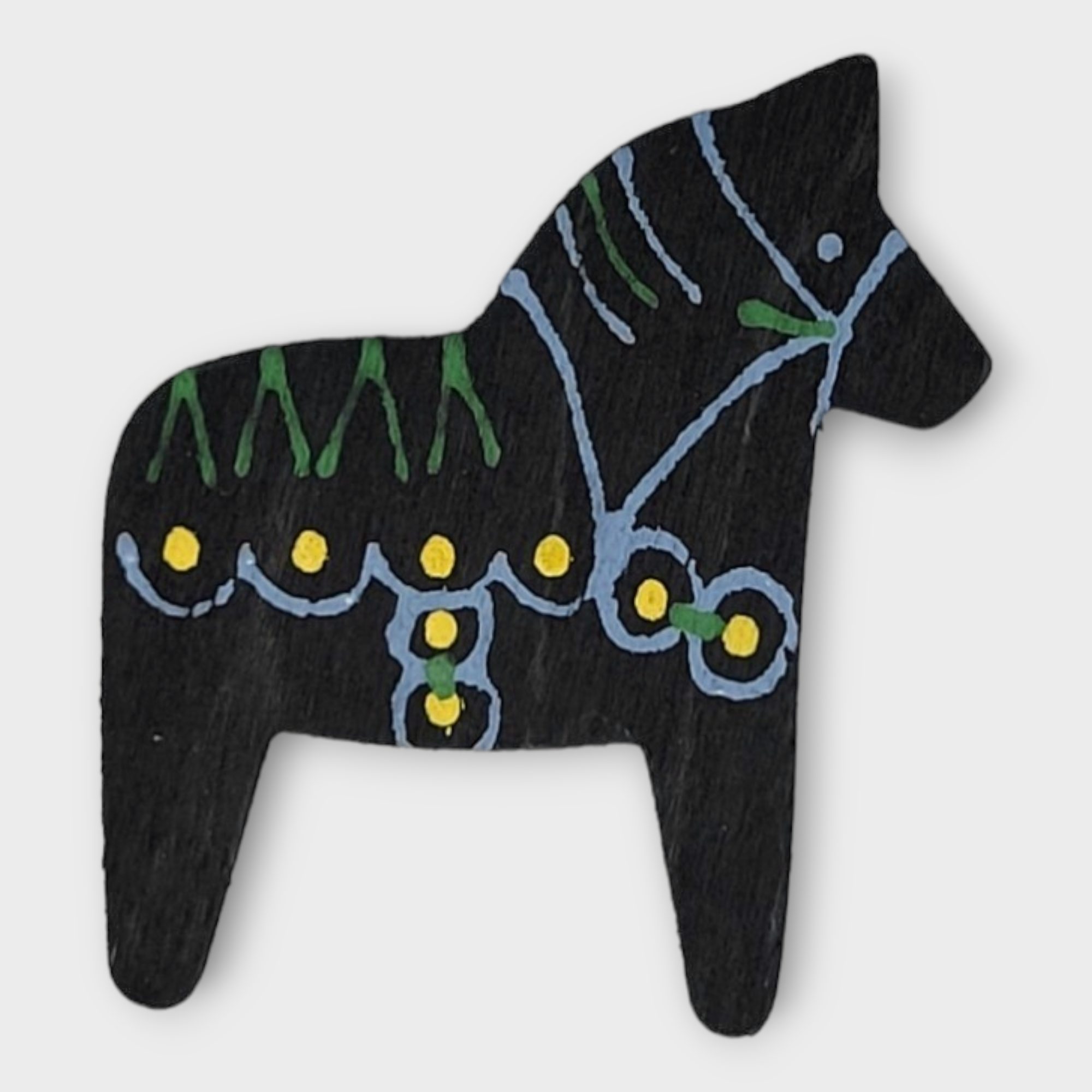 The Magnet: Dalahorse Black showcases a classic black Dala horse embellished with green and yellow designs against a white backdrop, capturing the essence of Scandinavian design and honoring Swedish tradition.