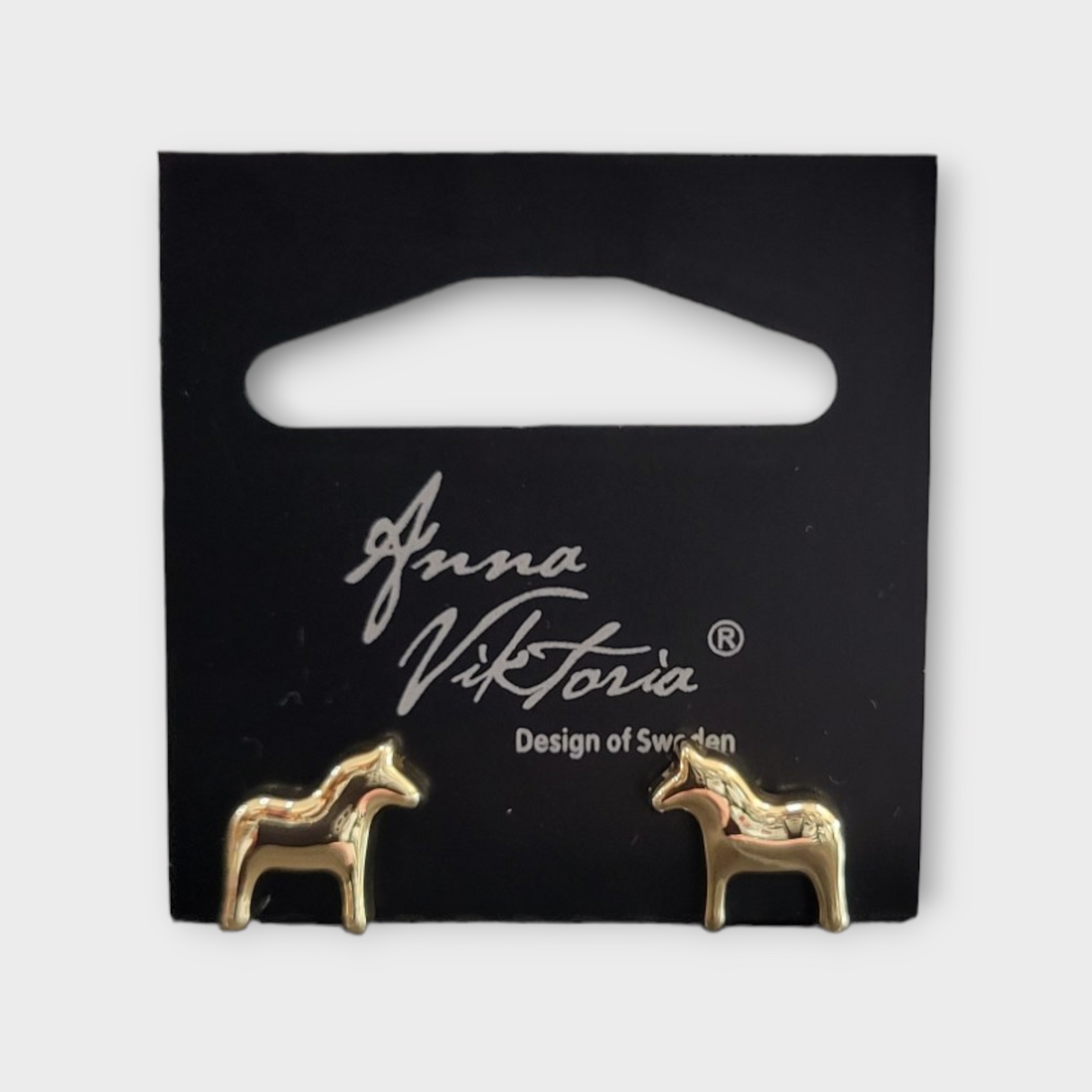 Gold horse-shaped earrings on a black card labeled Anna Viktoria, Design of Sweden. The Dala Earrings capture the essence of Scandinavian jewelry, blending Swedish charm with exquisite craftsmanship.