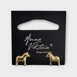 Gold horse-shaped earrings on a black card labeled Anna Viktoria, Design of Sweden. The Dala Earrings capture the essence of Scandinavian jewelry, blending Swedish charm with exquisite craftsmanship.