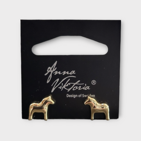Gold horse-shaped earrings on a black card labeled Anna Viktoria, Design of Sweden. The Dala Earrings capture the essence of Scandinavian jewelry, blending Swedish charm with exquisite craftsmanship.