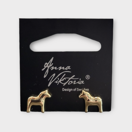Gold horse-shaped earrings on a black card labeled Anna Viktoria, Design of Sweden. The Dala Earrings capture the essence of Scandinavian jewelry, blending Swedish charm with exquisite craftsmanship.
