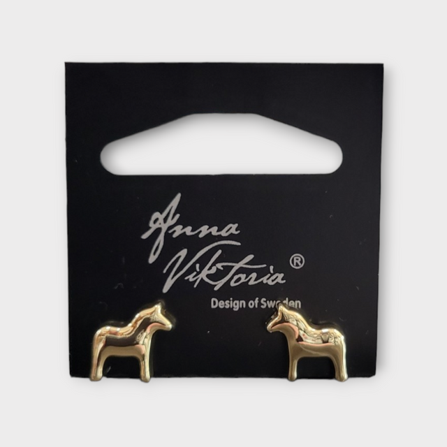 Gold horse-shaped earrings on a black card labeled Anna Viktoria, Design of Sweden. The Dala Earrings capture the essence of Scandinavian jewelry, blending Swedish charm with exquisite craftsmanship.