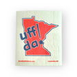 Introducing the "Dish Cloth: Uff Da - Lindstrom MN," designed with a red outline of Minnesota on a beige background and bold blue text reading "uff da." This eco-friendly, highly absorbent cloth displays SwedishGiftStore.com in the bottom left corner and Lindström, MN in the bottom right.